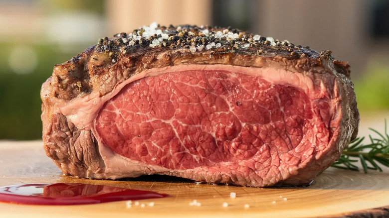 Cooked and seasoned prime rib roast with layer of fat on top.