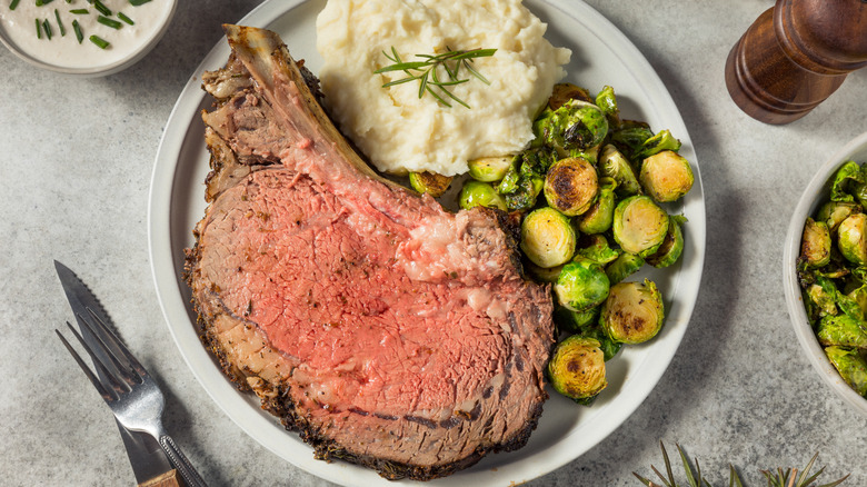 Homemade prime rib on plate with mashed potatoes and roasted Brussels sprouts.