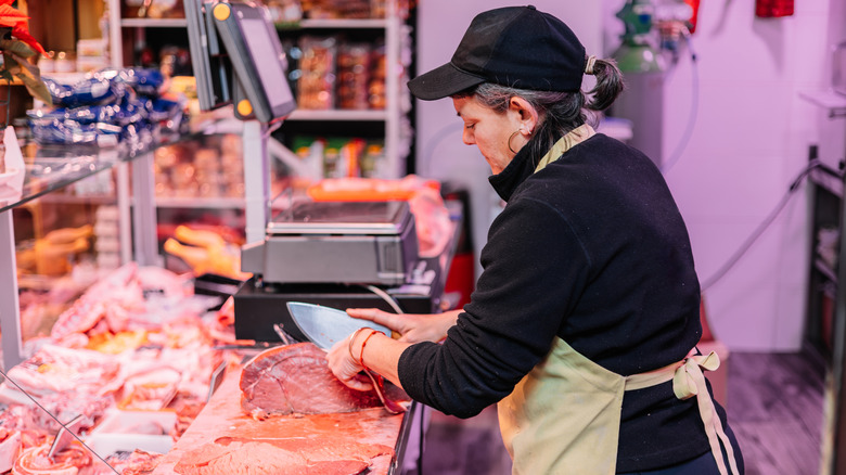 Butcher carving beef inside shop.