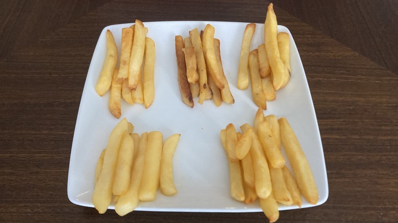 A white plate with five piles of fries cooked to varying levels of crispness