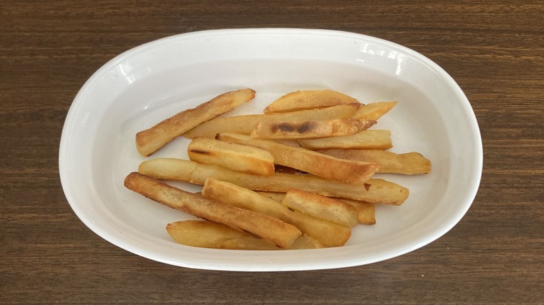 Crispy french fries some of which look overcooked in a white dish