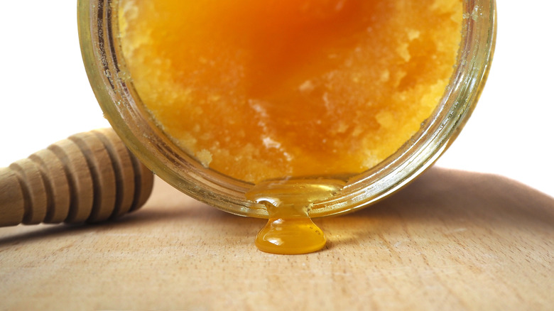Honey leaking from a jar of crystallized honey lying sideways on cutting board.