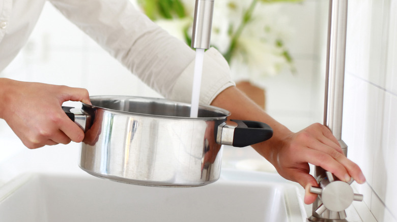 Person filling cooking pot at a sink.