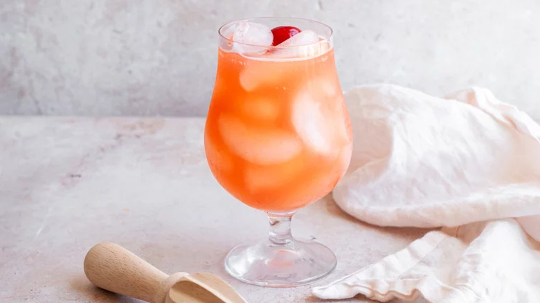 Pink-orange drink in cocktail glass with ice and cherry.