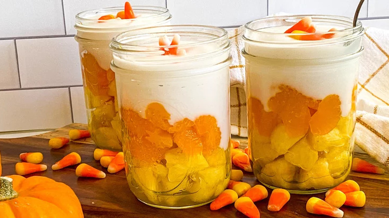 Mason jars with layered fruit, cream, and candy corn.