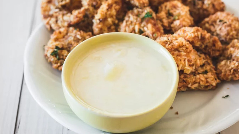 Small bowl of creamy white dip next to fried shrimp.