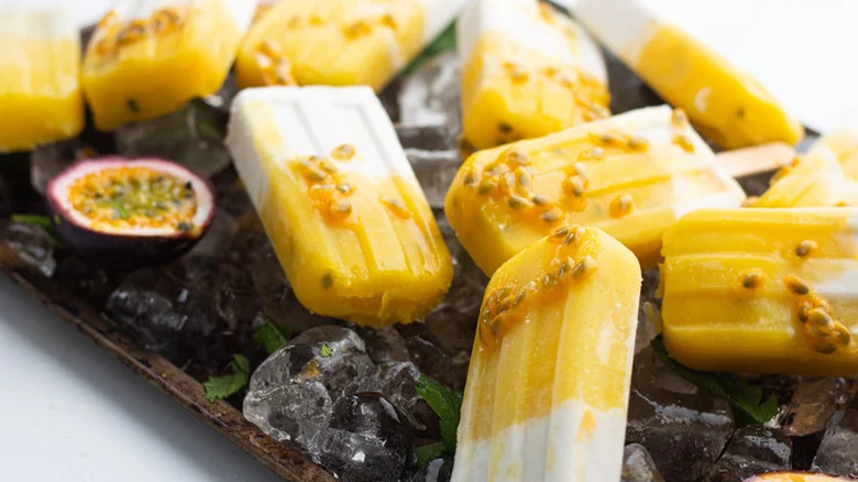 Yellow and white homemade popsicles on a tray of ice.