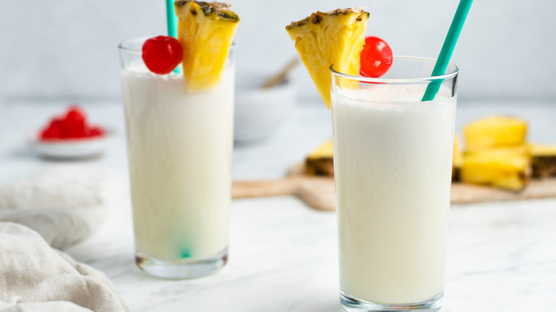 Two tall glasses of creamy pineapple cocktails with cherry garnishes.
