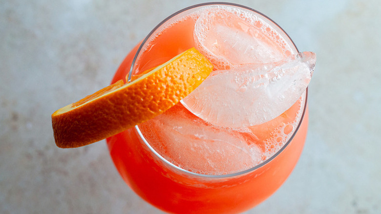 Glass of orange cocktail over ice with orange slice.