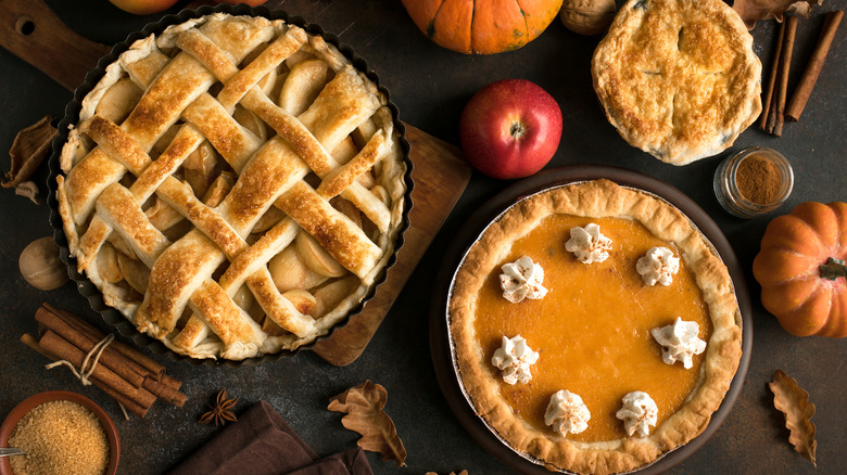 Large and small pies on table with apples and pumpkins.