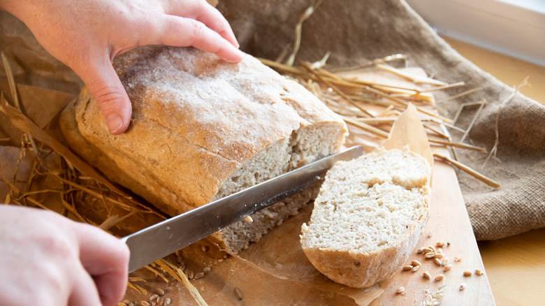 hands slice bread on cutting board with knife