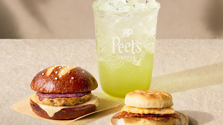 Peet's Coffee Sparkling Green Apple Energy drink with ice next to two sandwiches on a beige background