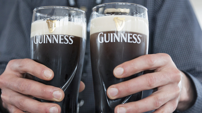 Person holding two pints of Guinness