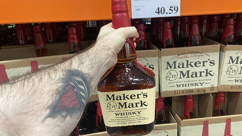 Arm holding Maker's Mark bottle beside Costco's boxed inventory