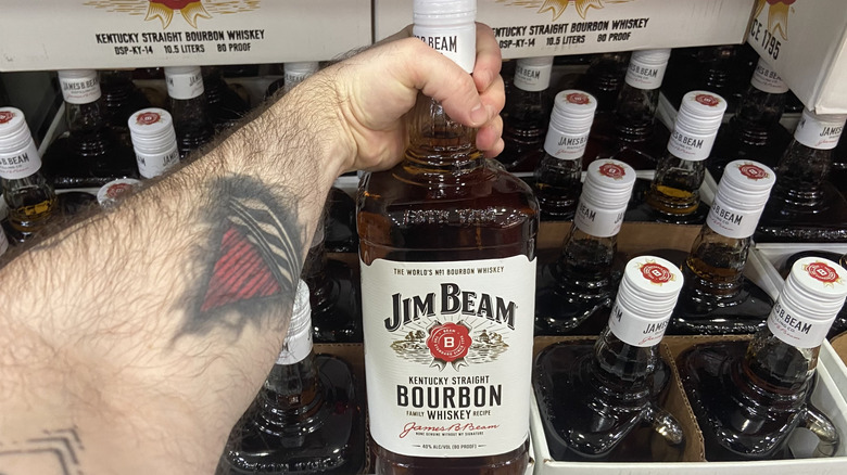 Arm holding a Jim Beam bottle beside Costco's boxed inventory