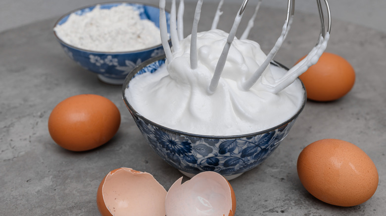 Beaten egg whites with stiff peaks in blue floral bowl next to brown eggs.