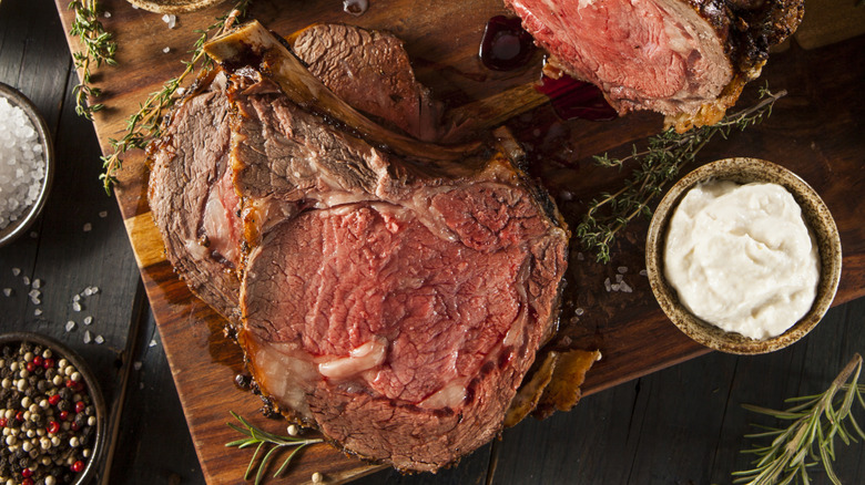 Partially sliced prime rib on cutting board with small bowl of horseradish.