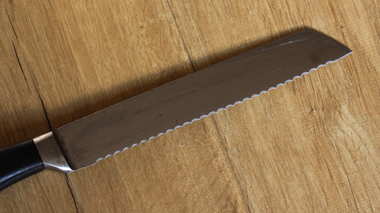 Closeup of serrated metal knife with black handle on wood surface.