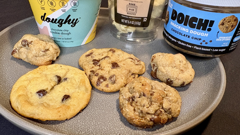 A variety of chocolate chip cookies on a plate with several packages of dough behind