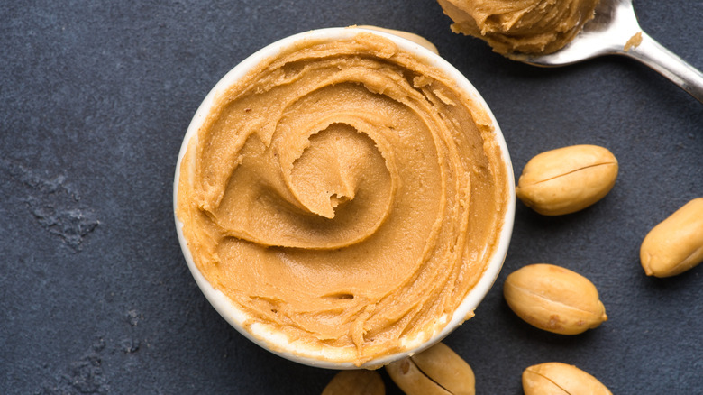 bowl of fresh peanut butter swirled with spoon next to peanuts