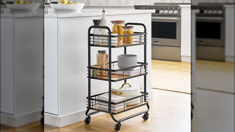 Rolling black bar cart holding various ingredients, bakeware, and towels in kitchen.