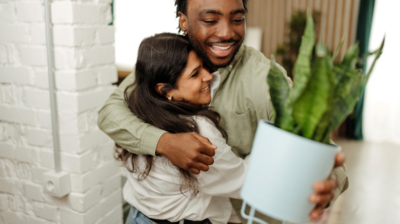 Woman hugging man at door, having handed over potted plant