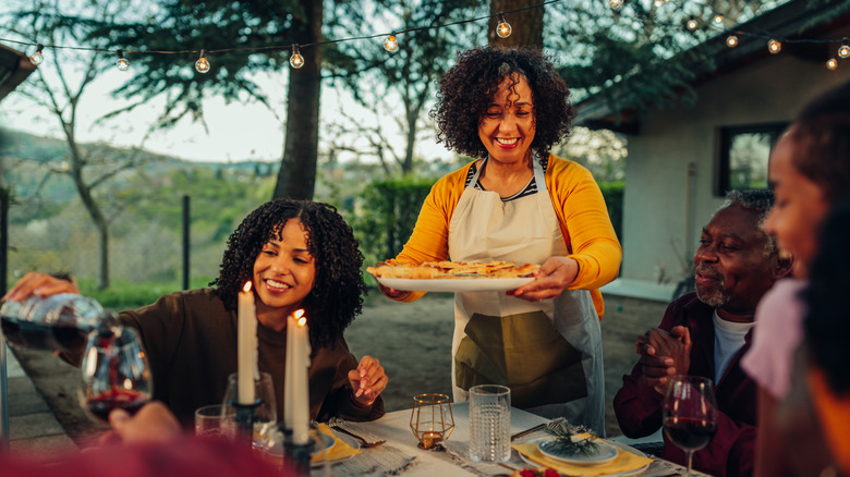 Woman bringing tray of food to table, where guests are gathered around