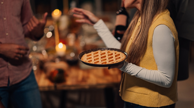 Woman holding pie with table in soft focus behind