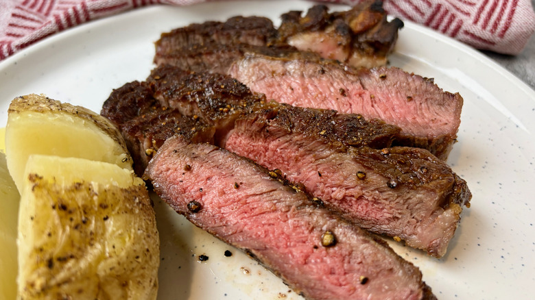 Slices of a cooked Trader Joe's Beef Rib Eye Steak on a plate with a baked potato.
