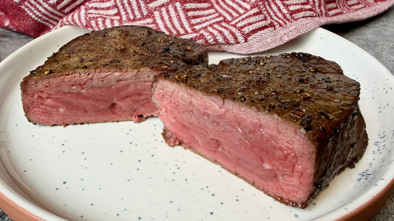 A cooked Trader Joe's Filet Mignon sliced in half and open to the pink center on a plate.