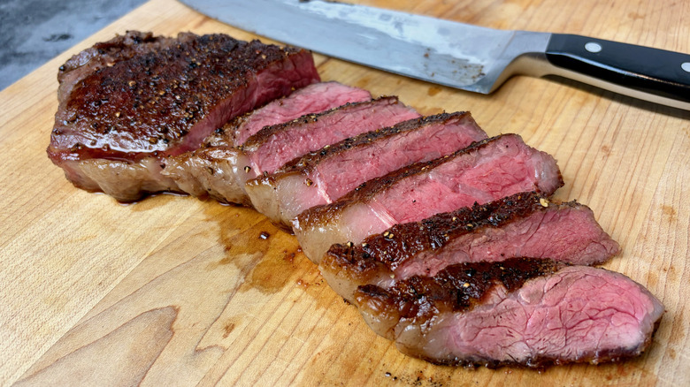 A cooked and sliced Trader Joe's New York Strip Steak on a cutting board with a knife.
