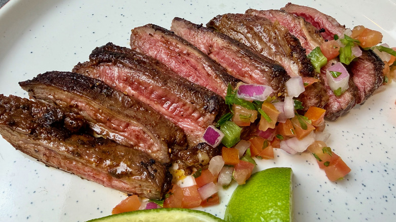 A cooked Outside Skirt Steak from Trader Joe's with pico de gallo and lime wedges.