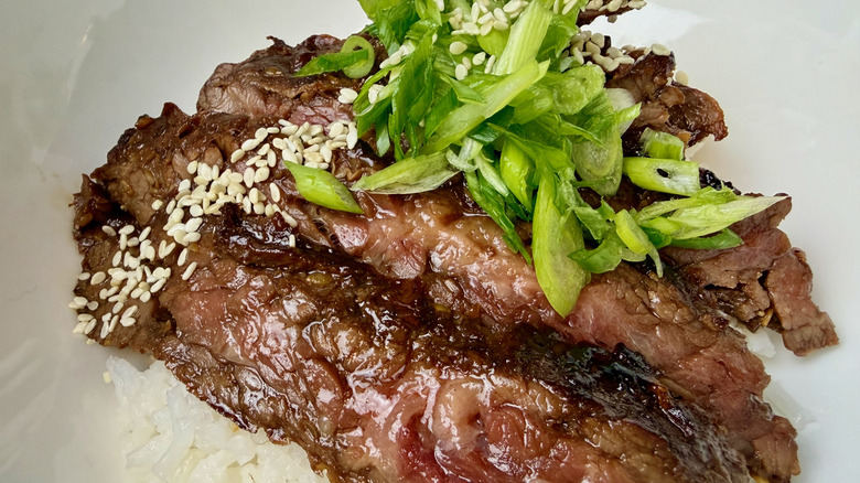 A cooked Trader Joe's Sesame Teriyaki Beef Skirt Steak with rice, scallions, and sesame seeds.