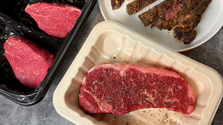 A small variety of Trader Joe's steaks, including raw filet mignon, raw and seasoned New York strip steak, and a cooked rib eye steak.