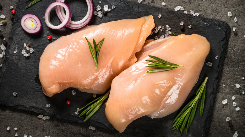 Raw chicken breasts on slate with herbs and onions