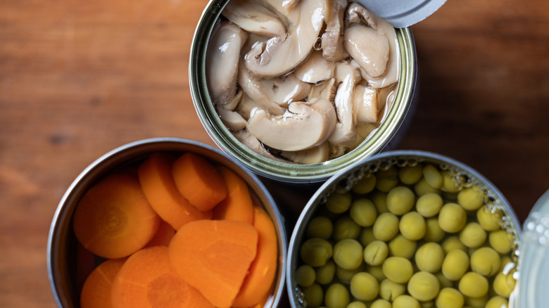Top-view of three open tin cans, each filled with sliced pickled mushrooms, carrots, and green peas