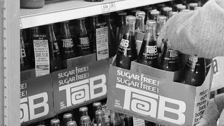 Black and white photo of Tab sugar-free soda bottles in cardboard crates displayed on a store shelf