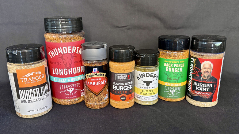 Seven burger spices lined up on a black background