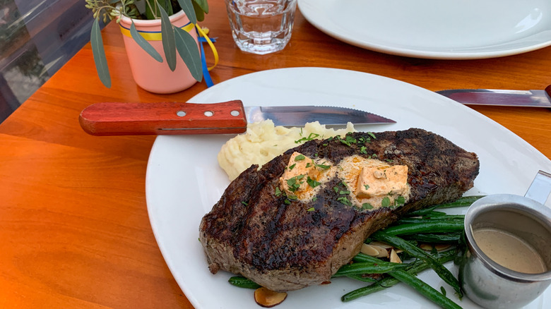 A plate of steak and a steak knife with a wooden handle at a restaurant