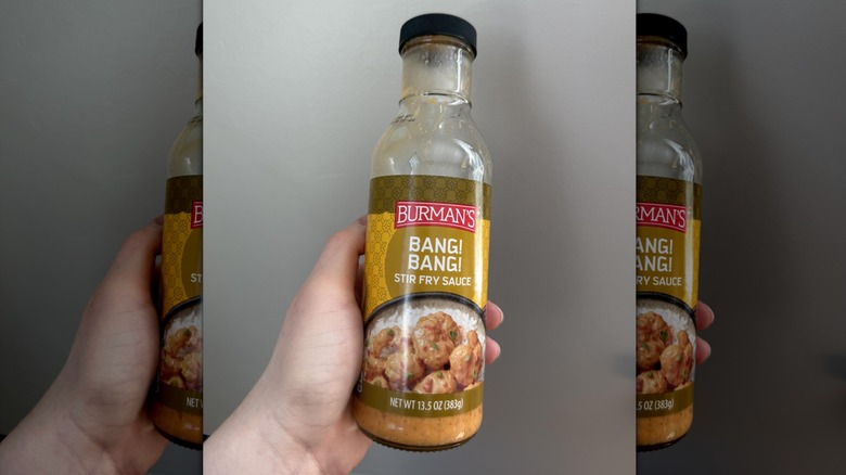 A hand holding a bottle of Burman's Bang Bang stir-fry sauce