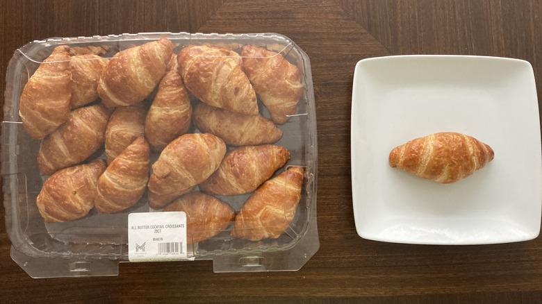 A box of croissants with one on a plate
