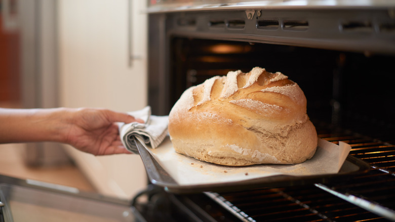 Hand taking a loaf of bread from the oven