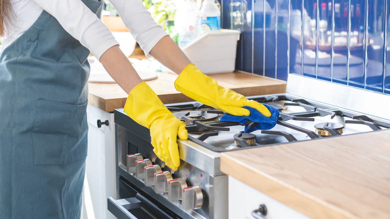 Person with yellow rubber gloves cleaning a gas stove