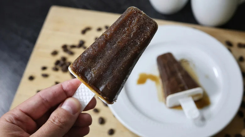 Hand holding a dark brown espresso martini popsicle.