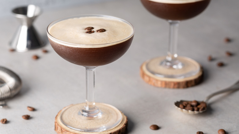 A frothy espresso martini in a round martini glass on a round wood coaster.