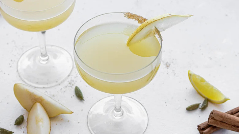 A light yellow martini with a partial brown sugar rim and a slice of pear garnish.