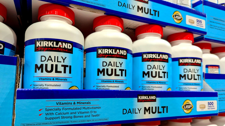 Bottles of Kirkland Signature Daily Multi vitamins are stacked on a Costco shelf.