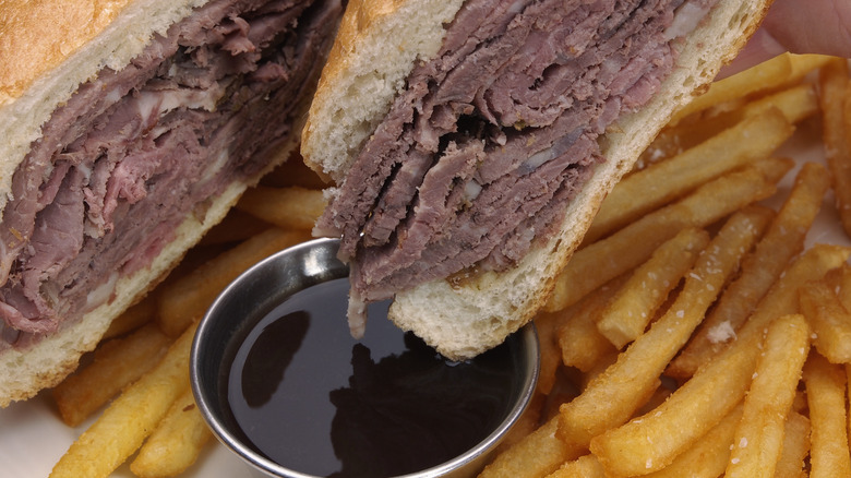 Bread, meat and cheese being dipped in au jus with French fries