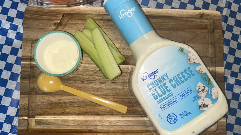 Bottle of Kroger blue cheese dressing with cucumbers and a yellow spoon