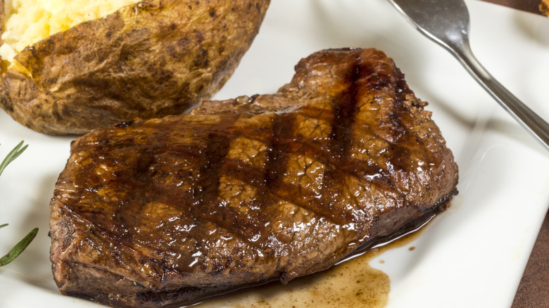 sirloin steak on a white plate with a baked potato